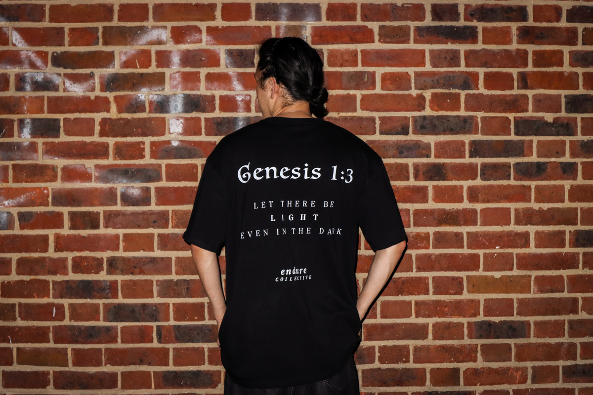 Black Genesis 1:3 oversized T-shirt back print photo featuring scripture-inspired “Let there be light even in the dark” design by ENDURE COLLECTIVE.