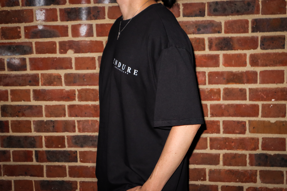 Black Genesis 1:3 oversized T-shirt front logo detail, featuring ENDURE COLLECTIVE chest print and faith-based streetwear design.
