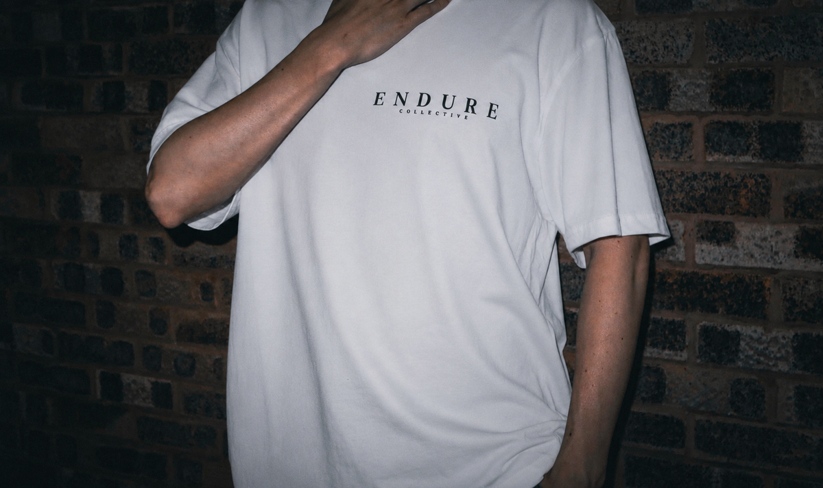 Model wearing White ENDURE COLLECTIVE oversized graphic T-shirt with minimal front logo