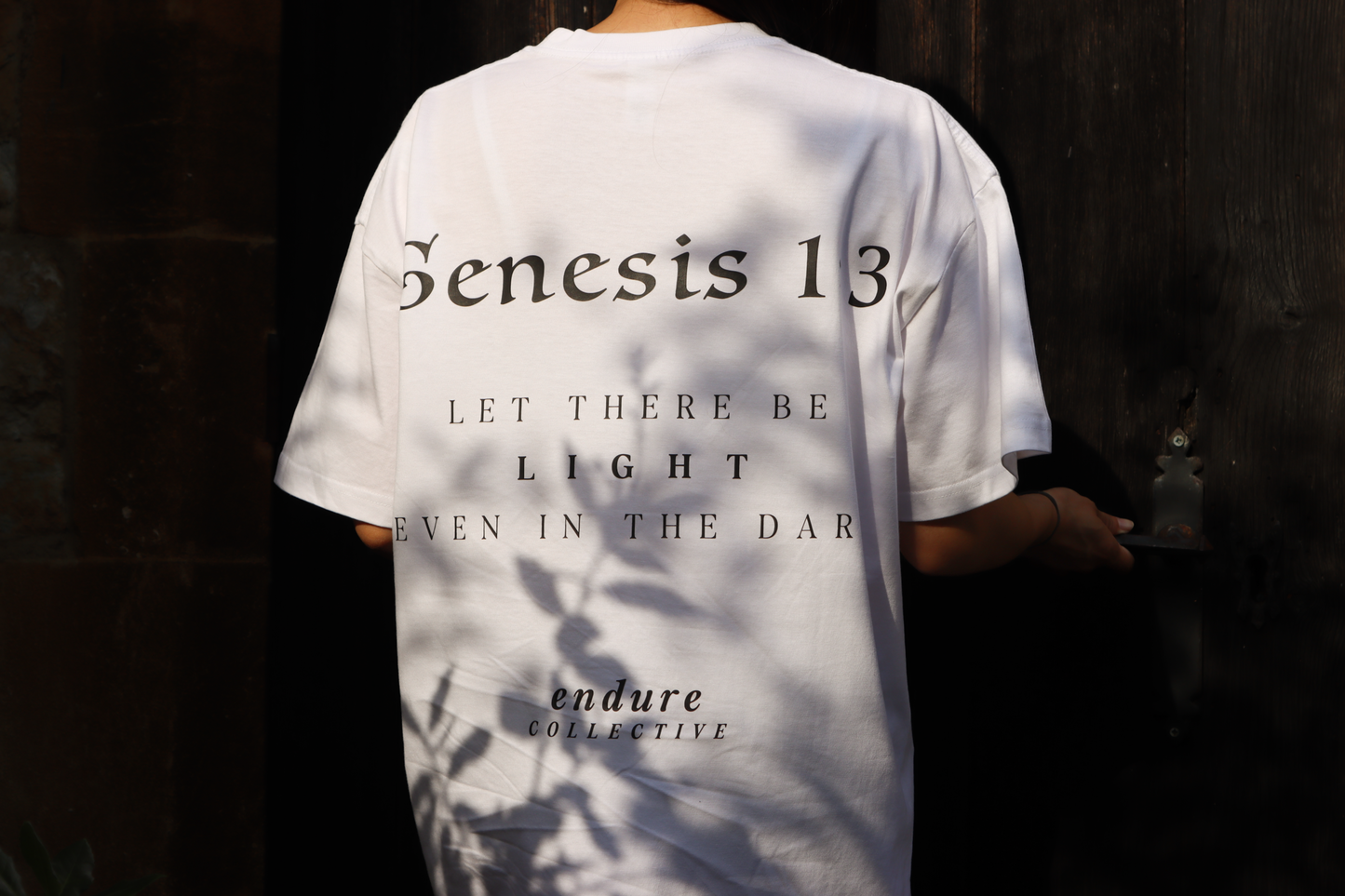 White Genesis 1:3 oversized T-shirt with black back print, featuring “Let there be light even in the dark” by ENDURE COLLECTIVE.