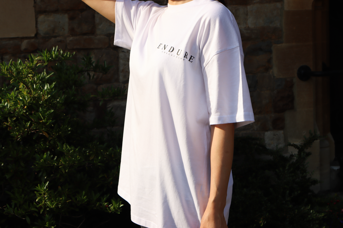 White Genesis 1:3 oversized T-shirt worn outdoors, featuring ENDURE COLLECTIVE front chest logo and faith-based streetwear design.